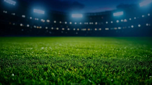 Football presentation background with a low-angle close-up of green stadium grass and blurred floodlights and bokeh under a deep blue night sky, in HD 16:9