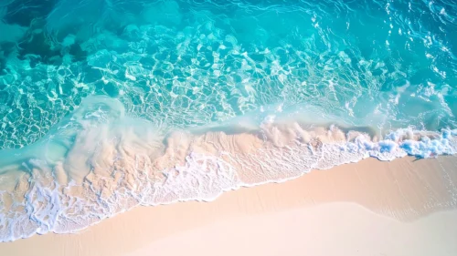 Aerial top-down beach background with rippling turquoise water and white foam meeting a sandy shore