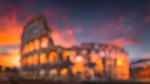 Colosseum background for PowerPoint, blurred Roman arches glowing amber under an orange and pink sunset sky